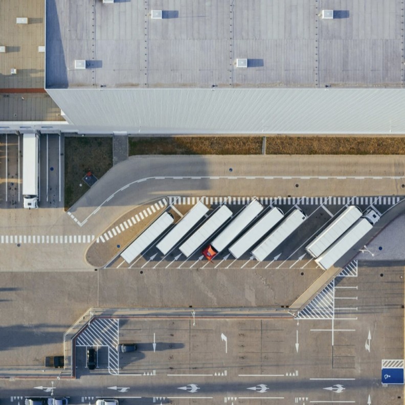 Aerial view of a logistics hub: warehouse roof, loading area and a row of parked trailers